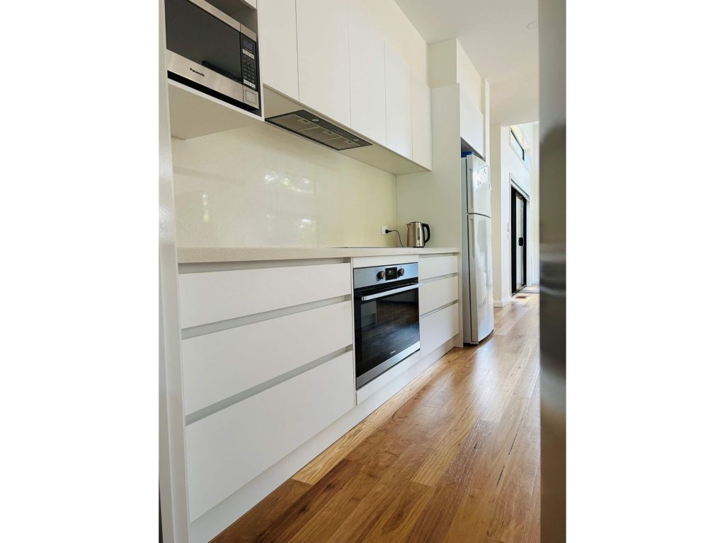 Kitchen with modern look and feel showcasing appliances like oven and microwave and handle free draw space storage