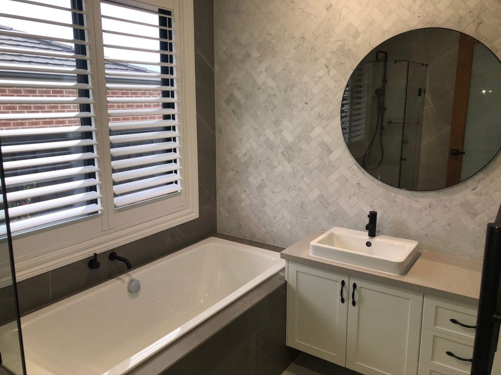Modern bathroom design with blinds and wide basin and cupboards and large circular mirror Officer
