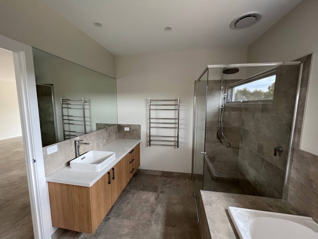 Modern bathroom renovation with wooden cabinet and white basin and bath with towel rack and large shower head and space
