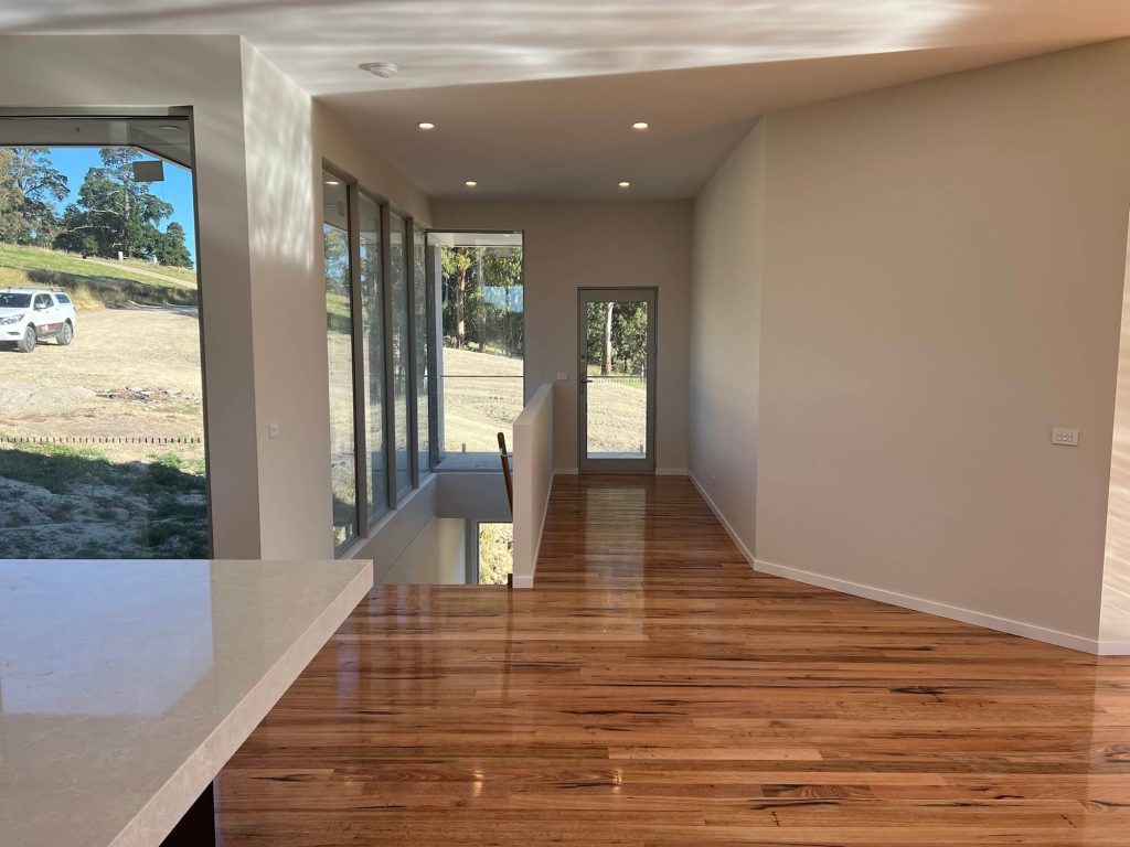 Open living space and staircase to downstairs intersecting with door access and kitchen space